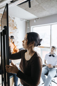 Young female entrepreneur writing on whiteboard in business meeting with colleagues at office