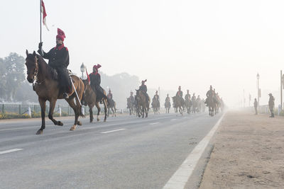 People riding horses on street against clear sky