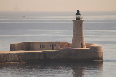 Lighthouse by sea against sky during sunset