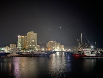 Sailboats in river by illuminated buildings against sky at night