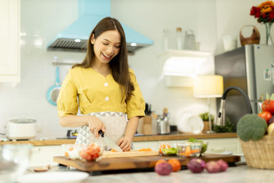 Smiling young woman preparing food in kitchen at home