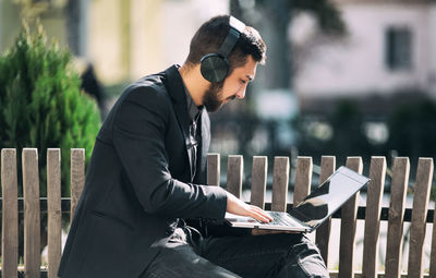 Side view of businessman using laptop while listening music on bench