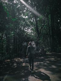 Rear view of man waking against trees while smoking