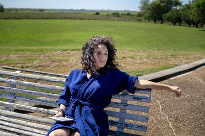 Woman relaxing sitting on a bench outdoors near swimming pool.