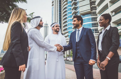 Multi-ethnic business colleagues looking at businessmen shaking hands against office