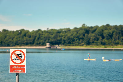 Warning sign by sea against blue sky