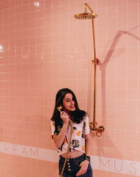 Portrait of young woman standing against wall at home