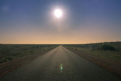 Road amidst field against sky during sunset