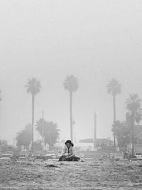 Woman sitting against palm trees and clear sky