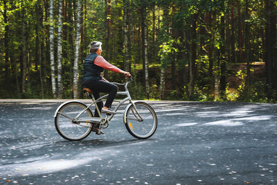 Side view of mature woman riding bicycle against trees