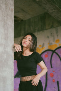 Portrait of young woman standing by wall