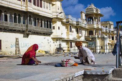 Man sitting by building against sky in city