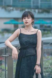 Portrait of young woman standing against railing