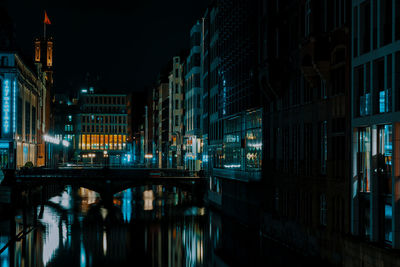 Illuminated bridge over canal by buildings in city at night