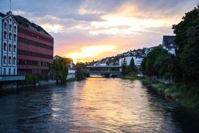 Bridge over river in city against sky at sunset