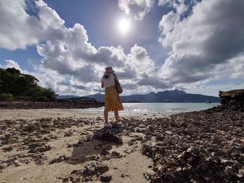 Rear view of woman standing on beach against sky