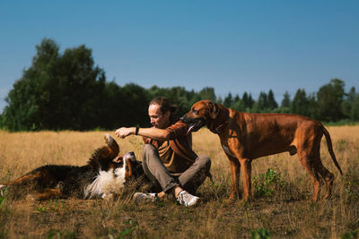 Man playing with dogs on land against sky