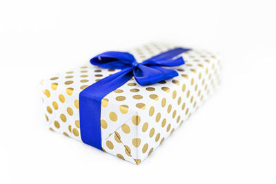 A gift wrapped in white paper with gold circles wrapped in a blue ribbon tied in a bow, isolated.