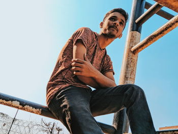 Low angle view of young man sitting against sky