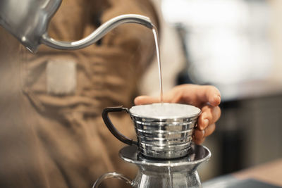 Cropped image of barista pouring water in coffee cup at cafe