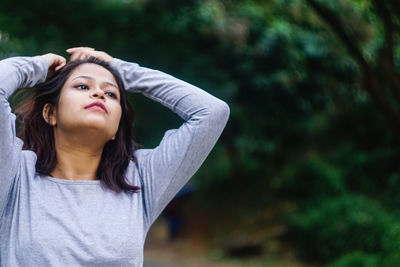 Thoughtful woman with hand in hair standing at park