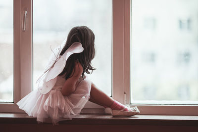 Girl wearing costume looking through window at home