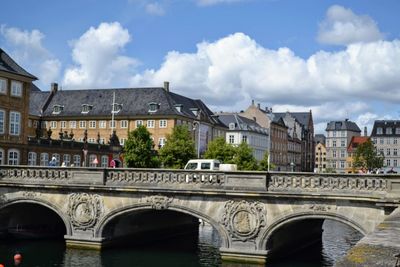 Arch bridge over river by buildings against sky in city