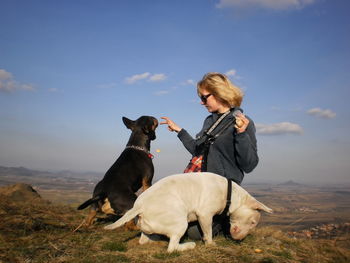 Woman feeding two dogs against the sky