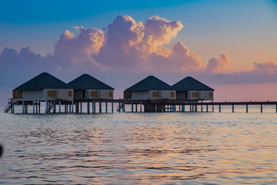 Stilt houses in sea against sky during sunset