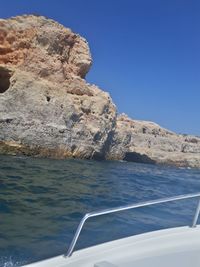 Rock formations by sea against clear blue sky