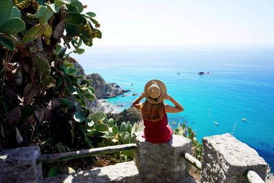 Panoramic view of young woman sitting on wall in capo vaticano, calabria, italy