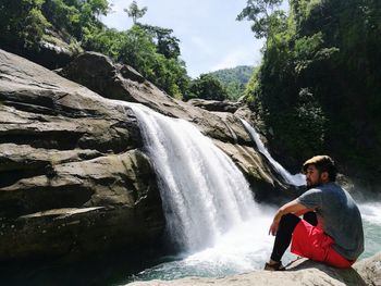 Man sitting in front of waterfall at forest