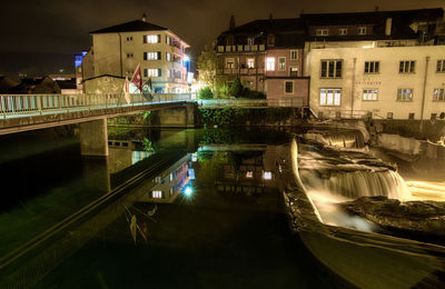 Bridge over canal amidst buildings in city at night