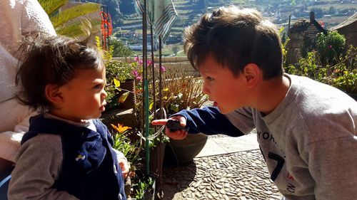 Boy talking to brother while standing at yard on sunny day