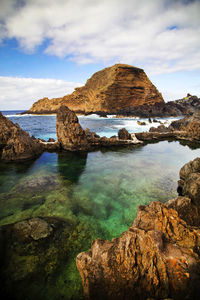 Rock formations on sea against cloudy sky