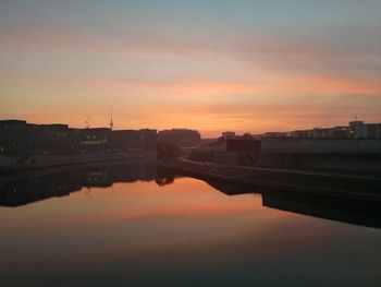 River by buildings against sky during sunset