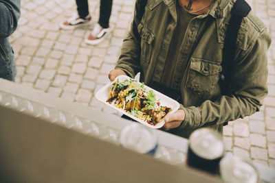 Midsection of male customer holding food plate by commercial land vehicle