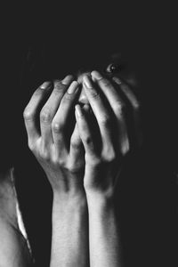 Close-up of young woman with hands covering mouth against black background