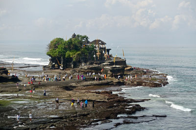 Wide view of a balinese hindu temple by the sea with many visitors. tanah lot, bali.