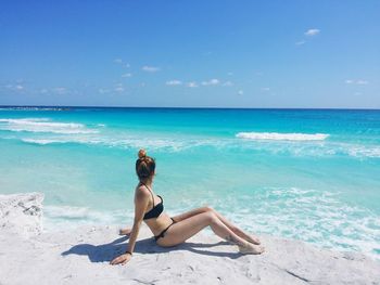 Full length of woman wearing bikini while sitting at beach against blue sky