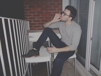 Young man smoking cigarette while sitting on chair at balcony