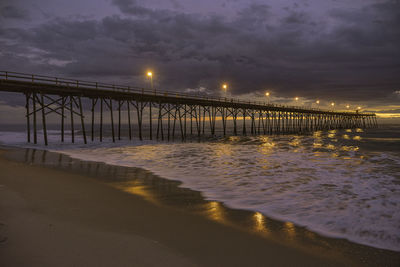 Illuminated bridge over sea against sky at night