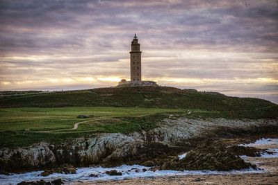 Lighthouse by sea against sky during sunset
