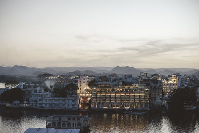 Buildings by river against sky during sunset