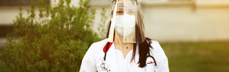 Woman wearing face shield standing against plant