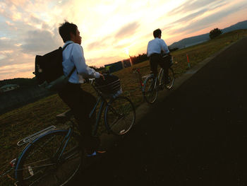 Rear view of people riding bicycle against sky during sunset