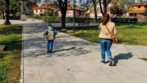 Rear view of mother and son walking on footpath