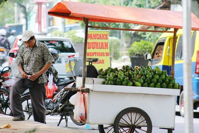 Full length of man standing by push cart filled with avocados at market