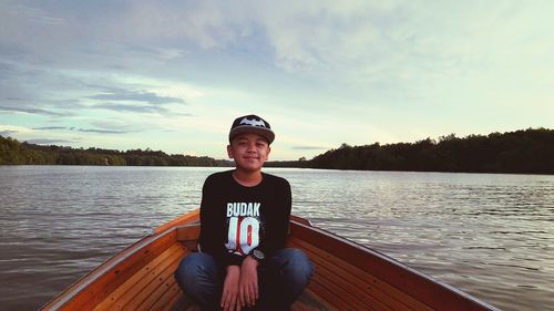 Portrait of smiling boy sitting on boat sailing in lake against sky