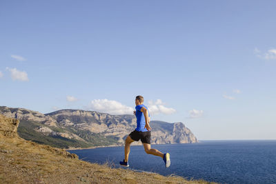 Male athlete running uphill trail on sky and sea background